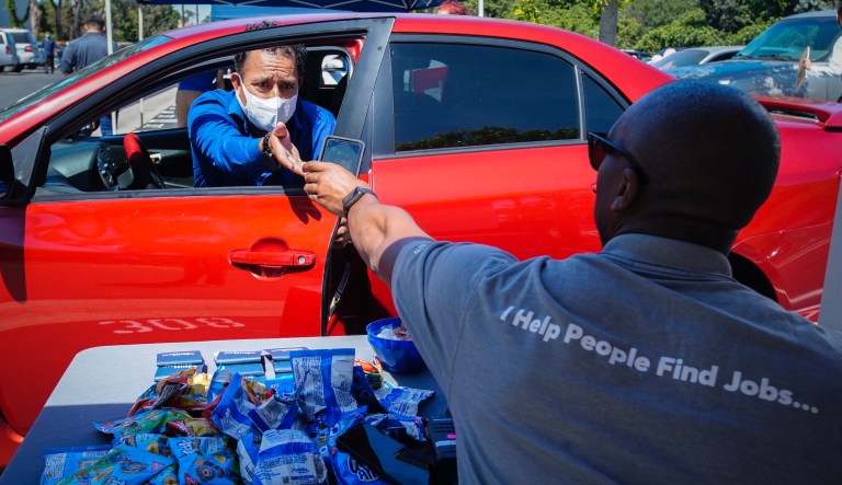 In this May 6, 2020, file photo, Brandon Earl, right, helps David Lenus, a job seeker, fill out an application at a drive up job fair for Allied Universal during the coronavirus pandemic, in Gardena, Calif. Coronavirus restrictions in California have put millions of people out of work, increasing the state's unemployment rate earlier this year to levels not seen since the Great Depression.