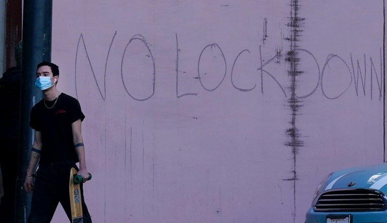 A person wearing a mask walks past writing on a wall reading "No Lockdown" during the coronavirus pandemic in San Francisco, Thursday, Dec. 17, 2020.