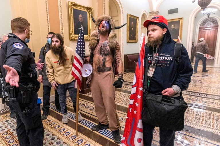 In this Wednesday, Jan. 6, 2021 file photo, supporters of President Donald Trump, including Jacob Chansley, center with fur hat, are confronted by Capitol Police officers outside the Senate Chamber inside the Capitol in Washington.  Right-wing extremism has previously mostly played out in isolated pockets of America or in smaller cities. In contrast, the deadly attack by rioters on the U.S. Capitol targeted the very heart of government. It brought together members of disparate groups, creating the opportunity for extremists to establish links with each other.