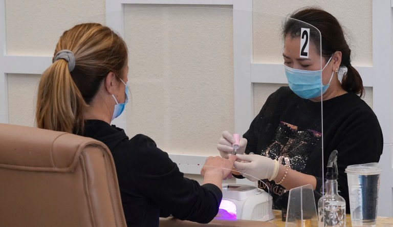 Sara Nguyen, right, sits behind a plexiglass shield as she gives a manicure to Christine Frazer at KB Nails in Sacramento, Calif., Monday, Jan. 25, 2021. 