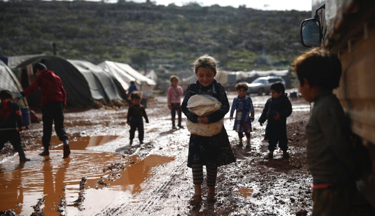 Syrian refugees walk through a camp for displaced muddied by recent rains near the village of Kafr Aruq , in Idlib province, Syria, Thursday, Jan. 28, 2021.