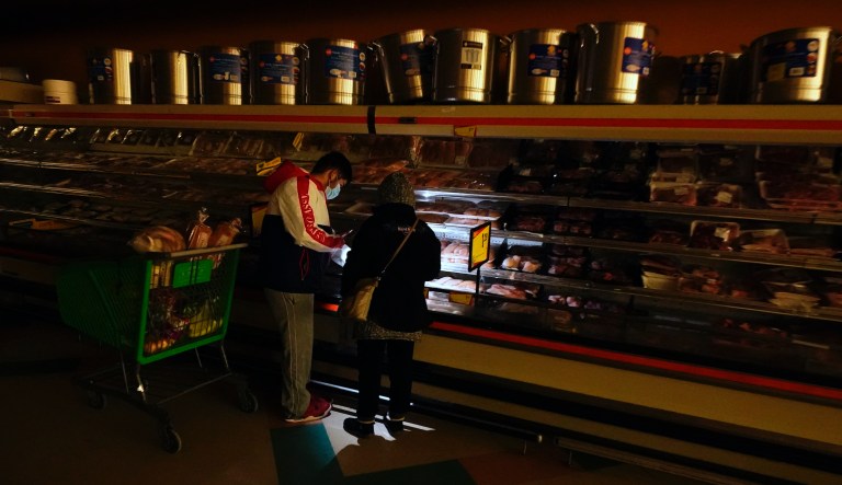 In this Feb. 16, 2021, file photo, customers use the light from a cell phone to look in the meat section of a grocery store in Dallas. Even though the store lost power, it was open for cash only sales.