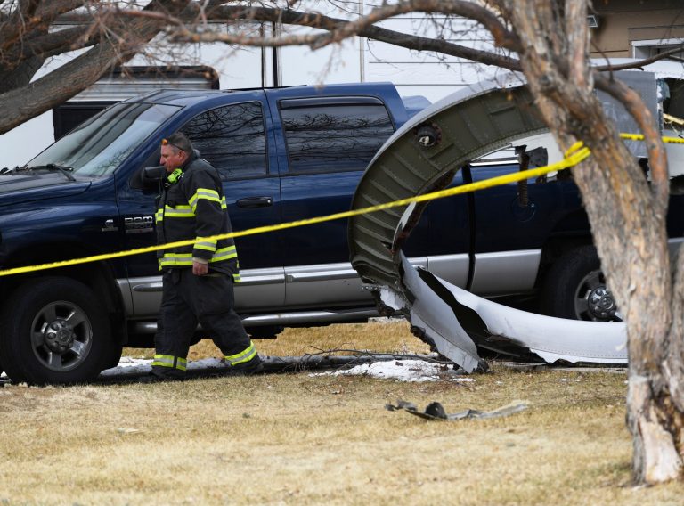 A North Metro firefighter walks past a large piece of an airplane engine in the front yard of a home on Elmwood Street near E. 13th Avenue, Saturday, Feb. 20, 2021, in Broomfield, Colo. (Andy Cross/The Denver Post via AP)