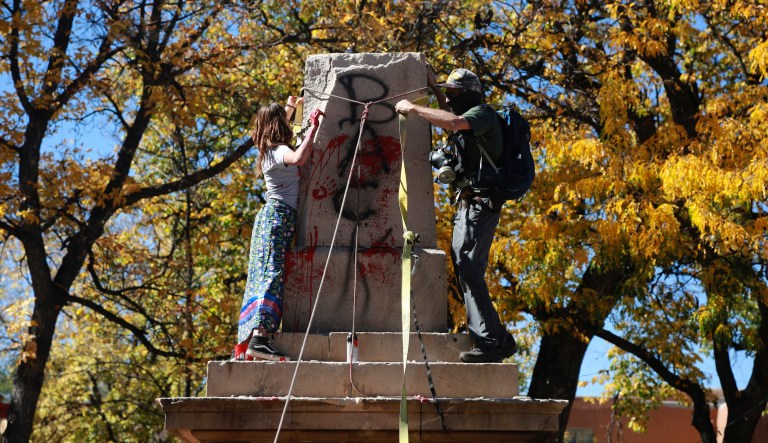 In this Oct. 12, 2020, file photo, demonstrators secure a rope around the centerpiece of a solid stone obelisk before tearing it down in Santa Fe, New Mexico.