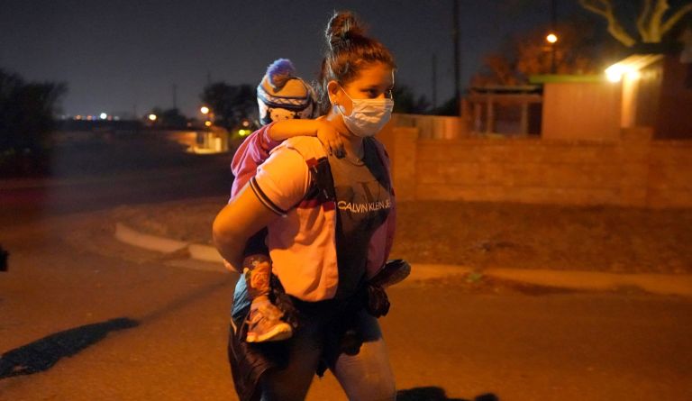 A migrant carries a child as her group follows an official to an intake area after turning themselves in upon crossing the U.S.-Mexico border, early Wednesday, March 24, 2021, in Roma, Texas. 