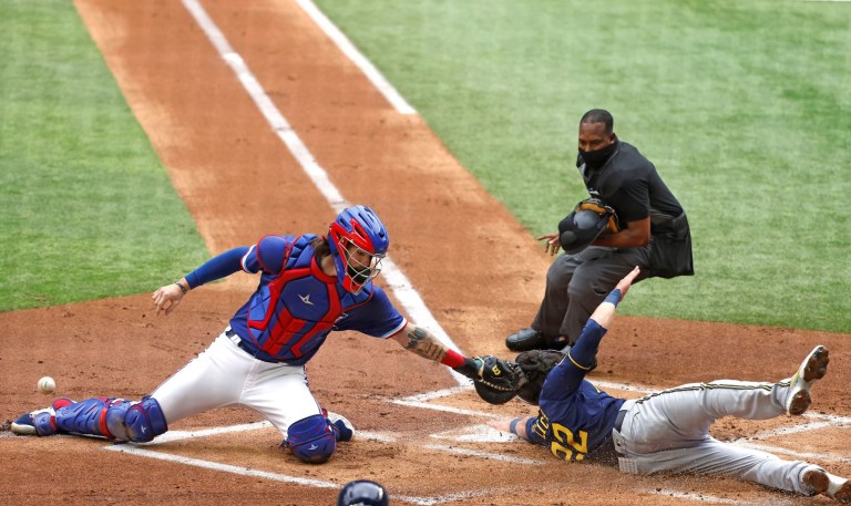 Milwaukee Brewers left fielder Christian Yelich (22) scores in front of Texas Rangers catcher Jonah Heim as home plate umpire Ramon De Jesus watches, during the first inning of a preseason baseball game Tuesday, March 30, 2021, in Arlington, Texas.