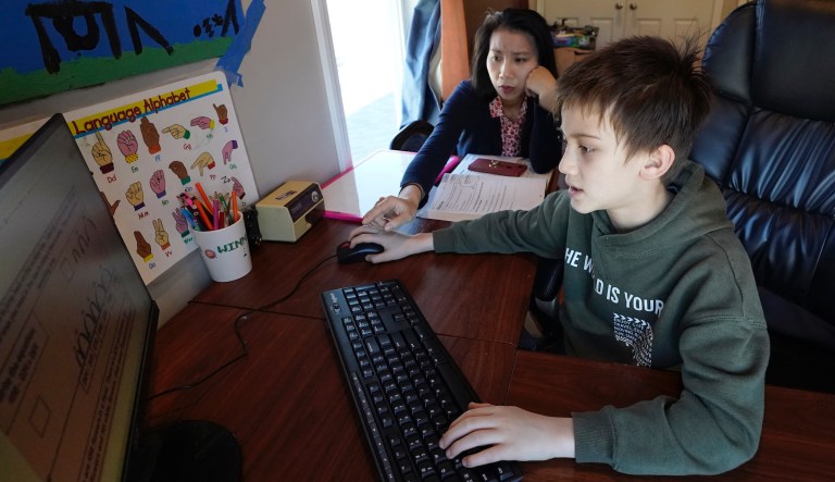 Kim Horrigan, left, sits with her son Conor Horrigan, 8, both of Quincy, Mass., as Conor does math homework at their home, in Quincy, Tuesday, April 13, 2021. Kim said she and her husband have struggled all year with their decision to keep their 8-year-old son in remote learning due to the coronavirus pandemic.