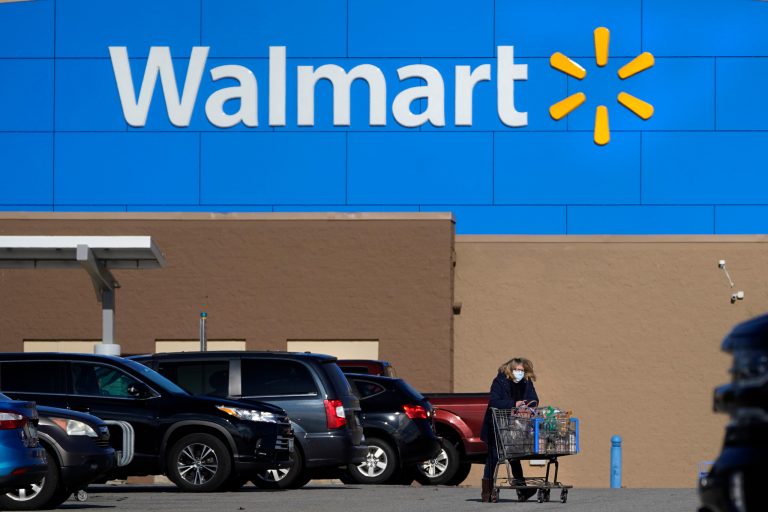 FILE - In this Nov. 18, 2020 file photo, a woman, wearing a protective face mask due to the COVID-19 virus outbreak, wheels a cart with her purchases out of a Walmart store, in Derry, New Hampshire. (AP Photo/Charles Krupa, File)