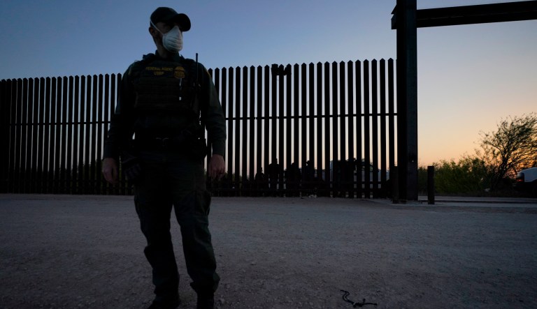 In this March 21, 2021 file photo, a U.S. Customs and Border Protection agent looks on near a gate on the U.S.-Mexico border wall as agents take migrants into custody, in Abram-Perezville, Texas.