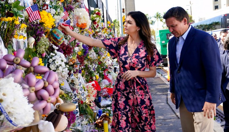 Florida Gov. Ron DeSantis, left, and his wife, Casey, leave flags at a makeshift memorial near the Champlain Towers South condo building.