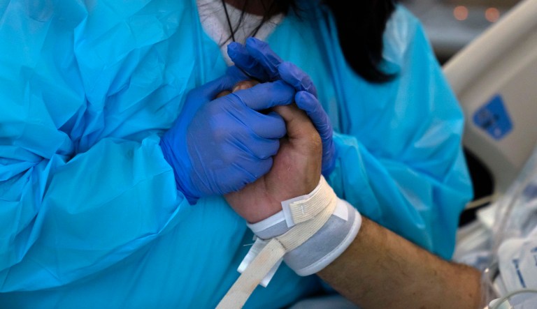Patty Trejo, 54, holds the hand of her intubated husband, Joseph, in a COVID-19 unit at St. Jude Medical Center, in Fullerton, Calif., Monday, Feb. 15, 2021. A summer coronavirus surge driven by the delta variant is again straining some hospitals particularly in rural areas of California, but the trend shows signs of moderating and experts say they expect improvement in coming weeks.                                                                                                                                                                                                                               