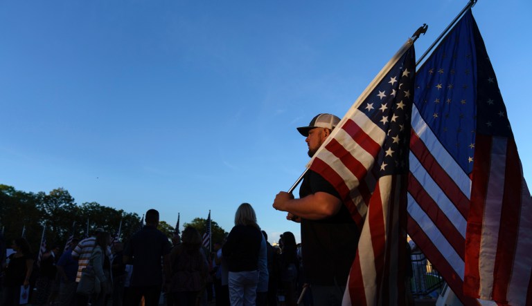 Josh Farrell holds American flags during a vigil Tuesday, Aug. 31, 2021, in the hometown of Lawrence, Mass., for Sgt. Johanny Rosario Pichardo, a U.S. Marine who was among 13 service members killed in a suicide bombing in Afghanistan.