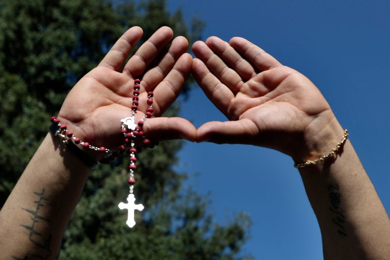 A supporter of Samir Geagea, the leader of the Christian Lebanese Forces party, holds a rosary and gives their sign, after Geagea declined to show up for questioning over deadly clashes in Beirut, outside his residence in Maarab east Beirut, Lebanon, Wednesday, Oct. 27, 2021. Geagea had been summoned by the military intelligence to give his testimony into the Oct. 14 clashes in south Beirut -- the worst the capital has seen in years -- that killed seven people and left several injured. (AP Photo/Bilal Hussein)