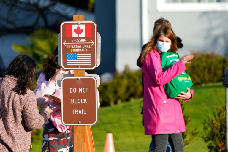 A woman in Canada waves to women talking between the U.S. and Canada border Monday, Nov. 8, 2021, in Blaine, Wash.