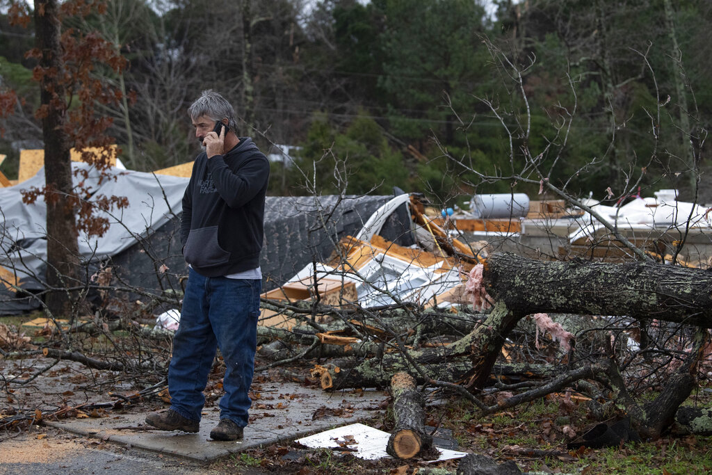Larry Rosenbaum uses his phone and surveys the damage as he stands outside a flattened home Saturday in Dickson County, Tennessee.