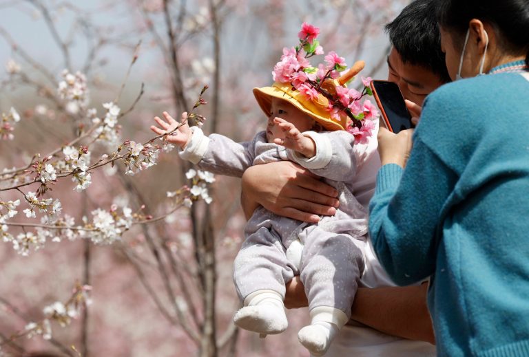 A man holds a child for photos near a cherry blossom tree in Beijing on March 24, 2021.