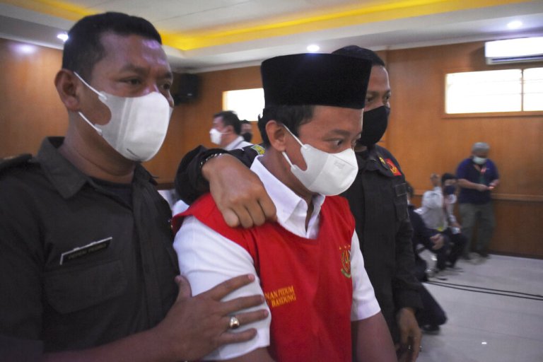 Herry Wirawan, center, the principal of a girls Islamic boarding school accused of raping his students, is escorted by security officers during a sentencing hearing at a district court in Bandung, West java, Indonesia, Tuesday, Feb. 15, 2022.