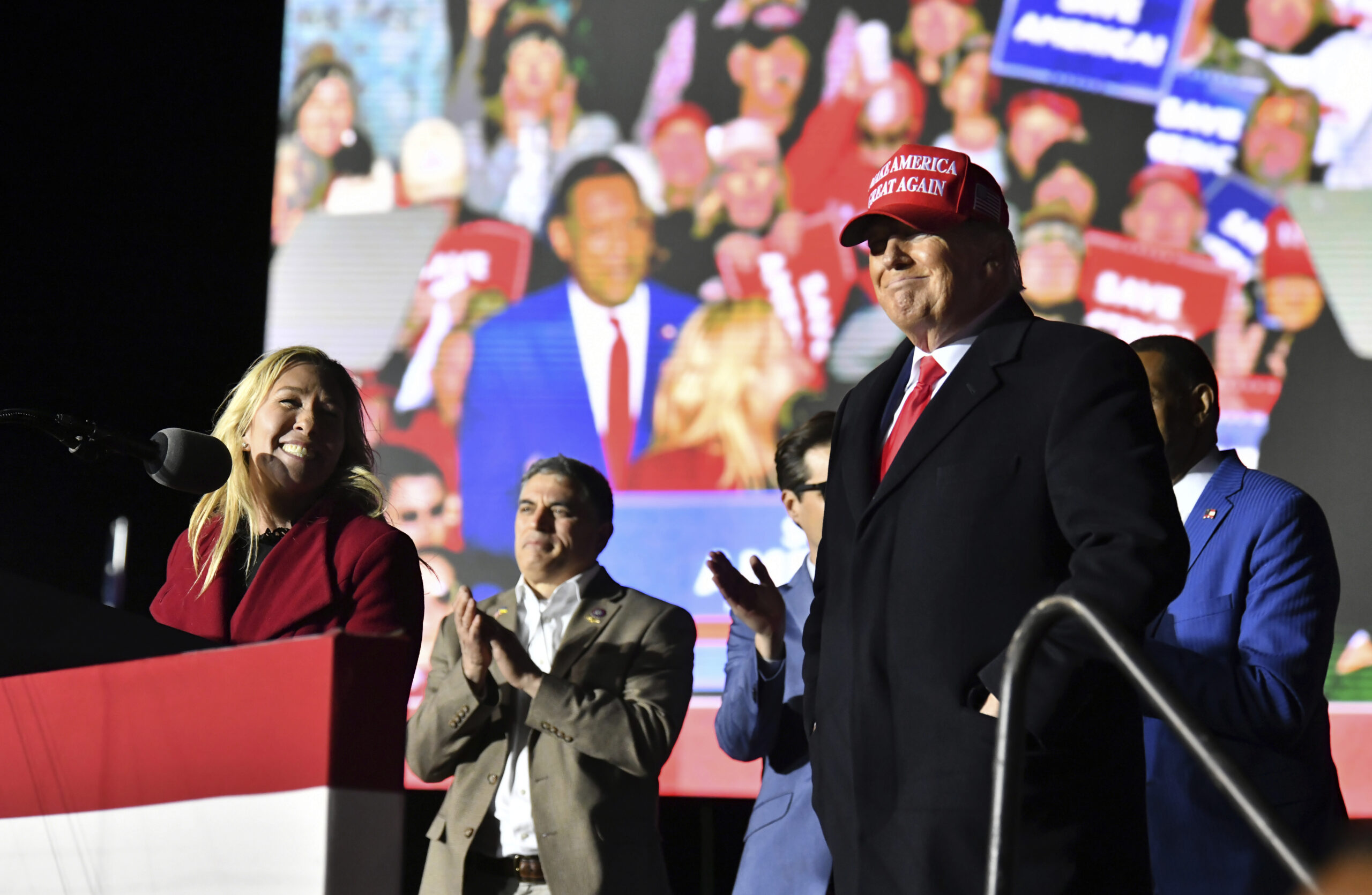Rep. Marjorie Taylor Greene, at the podium, thanks former President Donald Trump, right, during a rally for Georgia GOP candidates at Banks County Dragway in Commerce, Georgia, on March 26, 2022.