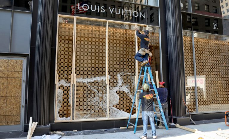 Workers begin to board up a display window at the Louis Vuitton store Monday, Aug. 10, 2020, after overnight vandals hit many high-end stores in Chicago.