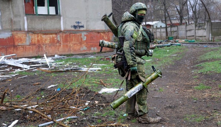 An armed serviceman of Donetsk People's Republic militia walks past a building damaged during fighting in Mariupol.