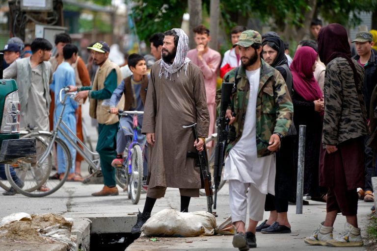 Taliban fighters stand guard as civilians gather at the site of an explosion in front of a school, in Kabul, Afghanistan, Tuesday, April 19, 2022. An Afghan police spokesman said explosions targeting educational institutions in Kabul have killed at least six civilians and injured over 10 others. Khalid Zadran said Tuesday the blasts occurred in the mostly-Shiite Muslim area in the west of Afghanistan's capital. 