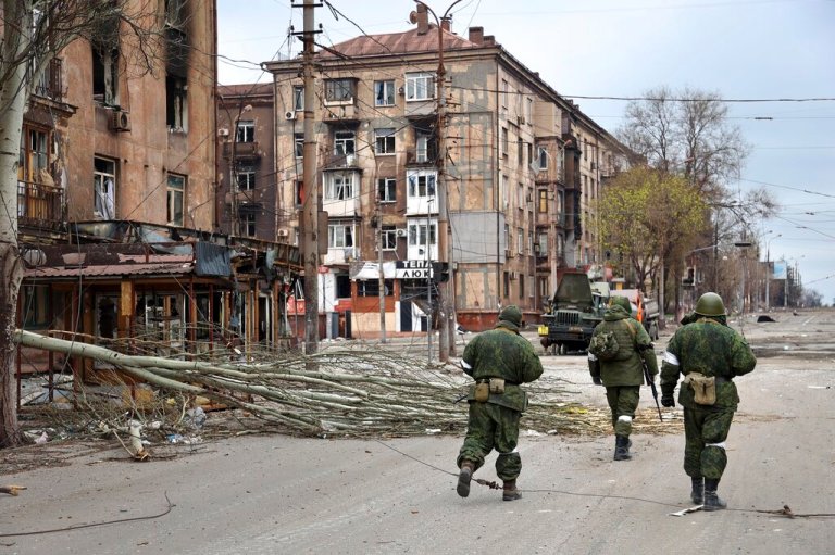 Servicemen of the militia from the Donetsk People's Republic walk past damaged apartment buildings near the Illich Iron & Steel Works Metallurgical Plant in an area controlled by Russian-backed separatist forces in Mariupol, Ukraine, Saturday, April 16, 2022. 