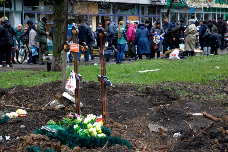 Local residents gather at a makeshift street market next to two fresh graves in the foreground in an area controlled by Russian-backed separatist forces in Mariupol, Ukraine, on Friday.