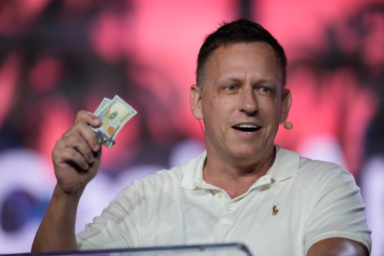 Peter Thiel, co-founder of PayPal and Palantir, offers a pair of hundred-dollar bills to attendees during a keynote address at the Bitcoin Conference, April 7, 2022, in Miami Beach, Fla.