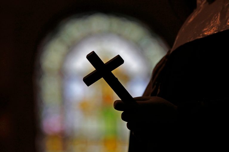 A silhouette of a crucifix and a stained glass window inside a Catholic church.