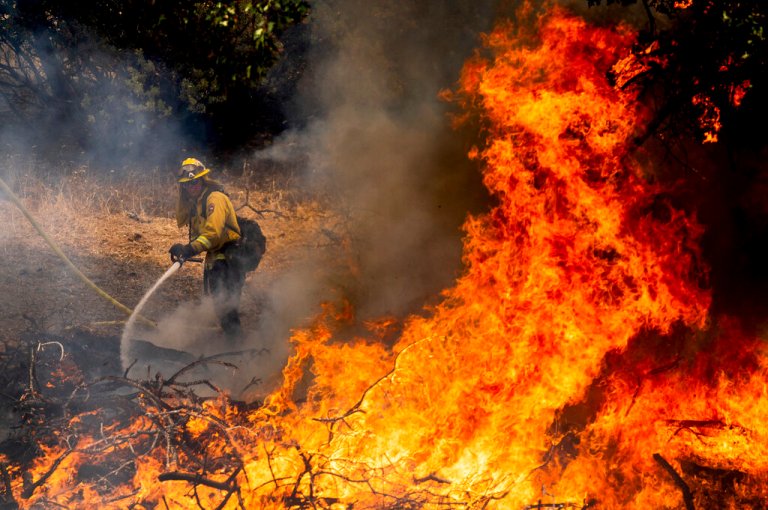 A firefighter sprays water while battling the Oak Fire in Mariposa County, California, on Saturday, July 23, 2022.
