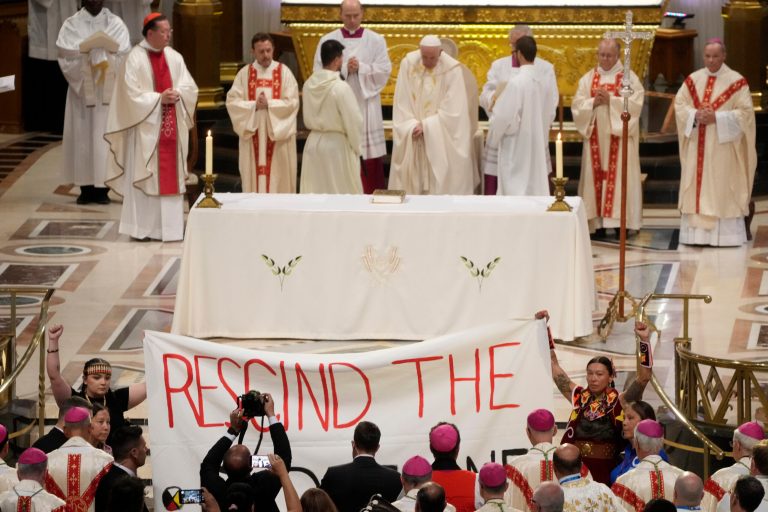Two protesters hold a banner during Pope Francis's mass at the National Shrine of Saint Anne de Beaupre in Quebec City, Canada, on Thursday, July 28, 2022. 