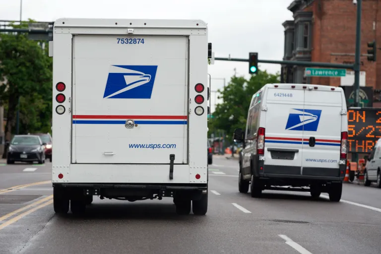 FILE - A USPS logo adorns the back doors of United States Postal Service delivery vehicles as they proceed westbound along 20th Street from Stout Street and the main post office in downtown Denver, Wednesday, June 1, 2022. (AP Photo/David Zalubowski, File)