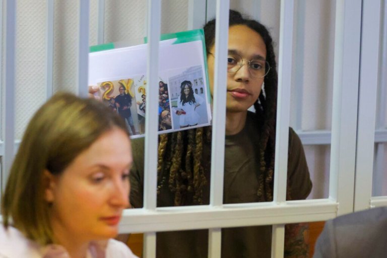 WNBA star Brittney Griner holds up images as she stands behind bars in a courtroom for a hearing, in Khimki, Russia, just outside Moscow, on Tuesday.