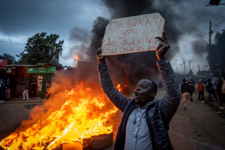 A supporter of presidential candidate Raila Odinga holds a placard next to a roadblock of burning tires in Nairobi, Kenya.