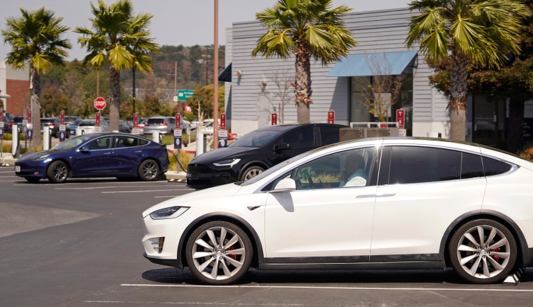 FILE - A man talks on his phone while sitting in his electric car at a Tesla charging station on Friday, April 2, 2021, in Marin City, California. Tesla's self-driving AI chip is expected to top the human brain (one quadrillion operations per second) in only 11 years by 2033, according to a new study. (AP Photo/Eric Risberg)