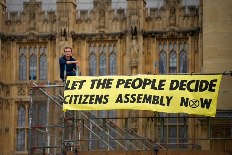 An Extinction Rebellion protester sits next to a banner outside the Palace of Westminster Friday, Sept. 2, 2022.