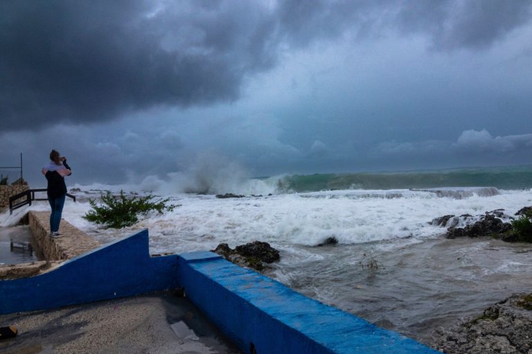 A woman takes photos while waves crash against a seawall as Hurricane Ian passes through George Town, Grand Cayman Island, Monday, Sept. 26, 2022. Hurricane Ian is on a track to hit the west coast of Florida as a major hurricane as early as Wednesday. 