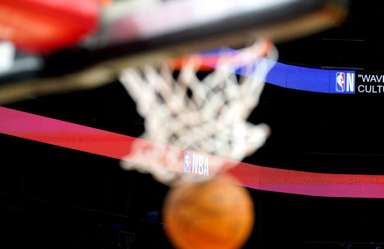 A basketball drops through the net with the NBA logo in the background.