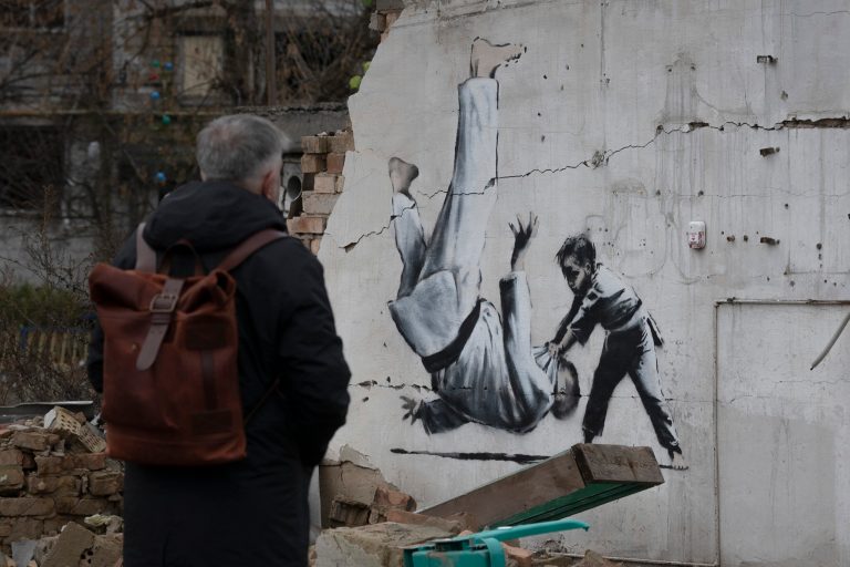 A man looks at a painting on a building destroyed by fighting in Borodyanka, Kyiv region, Ukraine, Sunday, Nov. 13, 2022. The artwork appears to have been made by British street artist Banksy, who confirmed on his Instagram account that he made another mural in the village that depicts a gymnast.