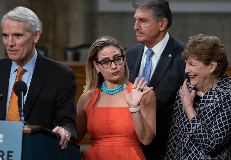 Sen. Kyrsten Sinema gestures during a news conference at the Capitol in Washington, Wednesday, July 28, 2021, while working on a bipartisan infrastructure bill with, from left, Sen. Rob Portman, Sen. Joe Manchin, and Sen. Jeanne Shaheen. 