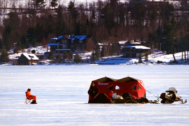 A fisherman sits in the sun outside a pop up shelter while ice fishing on frozen Lake Wentworth, Saturday, Feb. 11, 2023, in Wolfeboro, N.H. The Vermont Fish and Wildlife Department is warning people to stay off the ice on Lake Champlain due to unsafe conditions and an annual ice fishing derby was cancelled after three men fell through the ice and died this past week while ice fishing.
