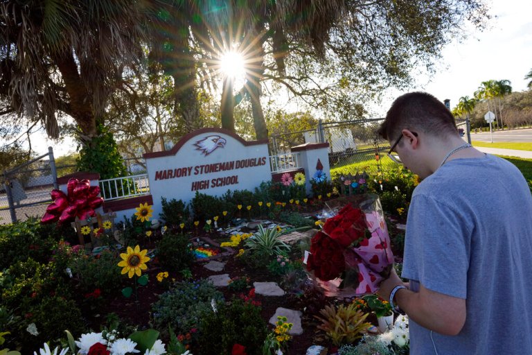 On the five-year anniversary of the shooting on Feb. 14, 2023, a person bearing flowers pays respects in front of a memorial for the 17 students and staff of Marjory Stoneman Douglas High School who were killed at the school in Parkland, Florida. 