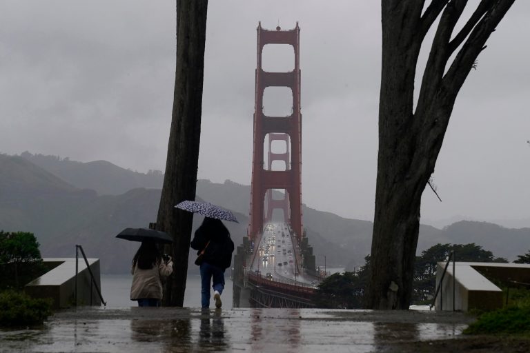 Traffic moves on the Golden Gate Bridge as people carry umbrellas while walking down a path at the Golden Gate Overlook in San Francisco, March 9, 2023.