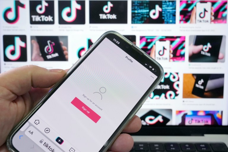 A sign up page for social media app TikTok is shown on a cell phone in front of a screen with logos for the company in Sydney, Tuesday, April 4, 2023. Australia had become the last of the Five Eyes security partners to ban the Chinese-owned app from government devices.