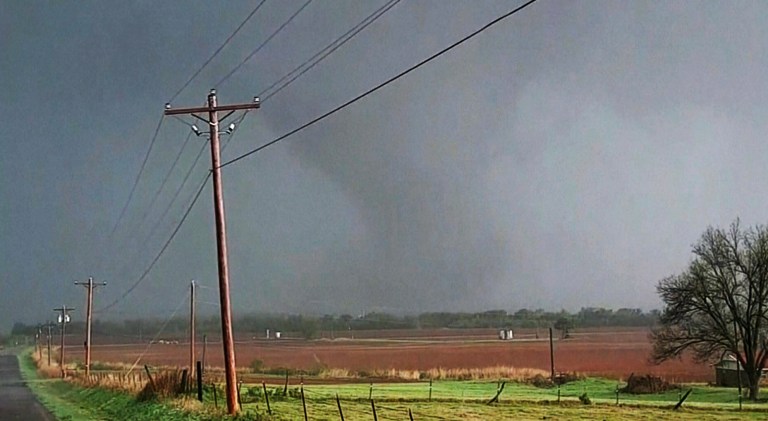 In this image taken from video, a massive funnel-shaped storm cloud makes its way over a road, as seen from a car, in Cole, Okla., Wednesday night, April 19, 2023. 