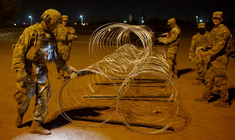 Texas National Guard soldiers tie rows of barbed wire to be installed near a gate in the border fence in El Paso, Texas, in the early hours of Thursday, May 11, 2023. Migrants rushed across the border hours before pandemic-related asylum restrictions were to expire Thursday, fearing that new policies would make it far more difficult to gain entry into the United States.