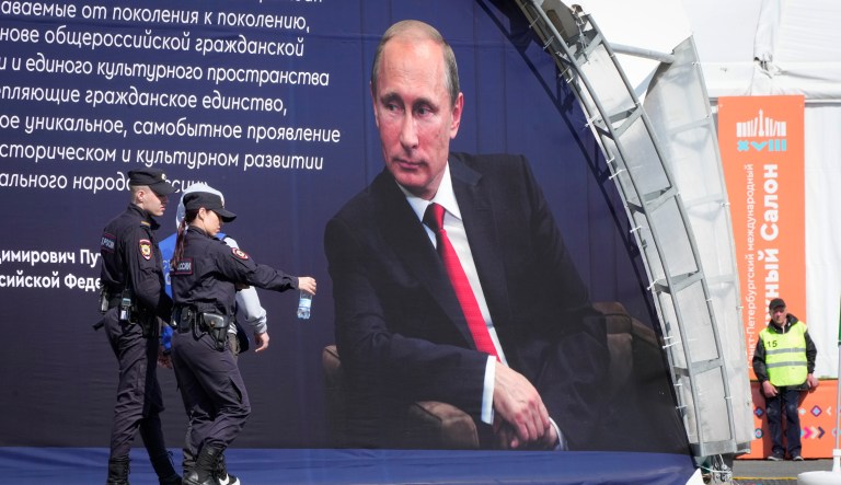 Police officers walk past a portrait of Russian President Vladimir Putin and a quote from his message at a book fair at the Dvortsovaya (Palace) Square in St. Petersburg, Russia, Sunday, May 21, 2023.