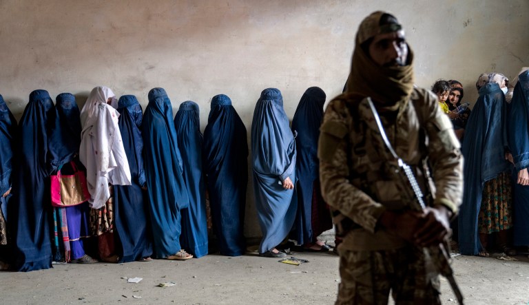 A Taliban fighter stands guard as women wait to receive food rations distributed by a humanitarian aid group, in Kabul, Afghanistan, Tuesday, May 23, 2023.