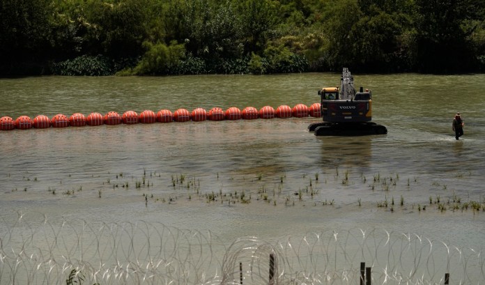 Workers deploy a string of large buoys to be used as a border barrier at the center of the Rio Grande.