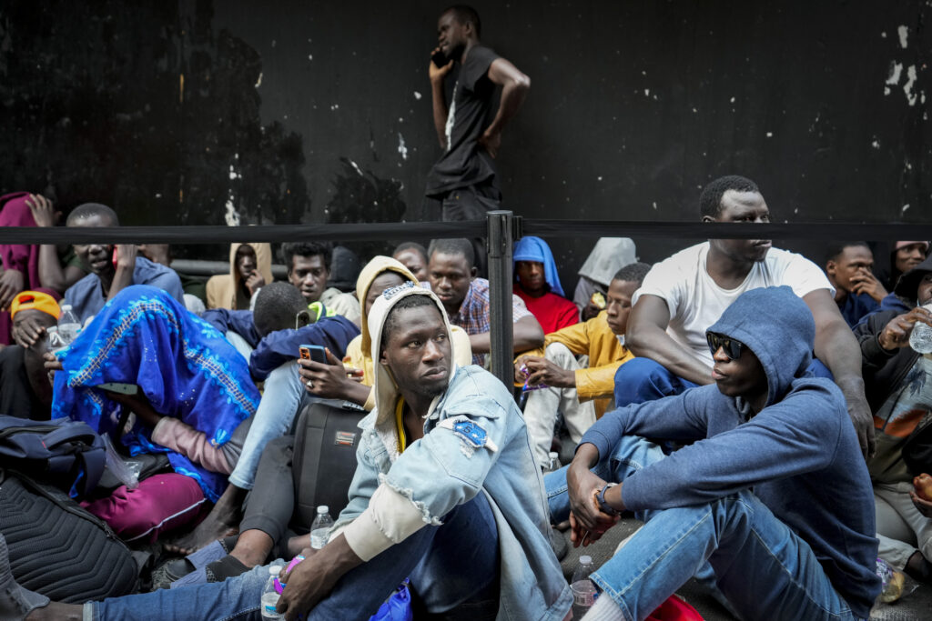 Immigrants sit in a queue outside of the Roosevelt Hotel that is being used by the city as temporary housing, July 31, 2023, in New York.